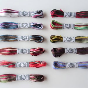 May include: Twelve spools of DMC embroidery floss in various colours and patterns. Each spool has a white label with the DMC logo and the word "Coloris" printed on it.