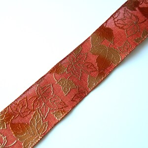 May include: A close-up of a red satin ribbon with a gold leaf pattern. The ribbon is ideal for adding a touch of elegance to any craft project.