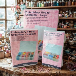 May include: Three pink Hemline embroidery thread organisers, labelled Large, Medium, and Small. Each box features a clear lid and contains colourful thread spools. Text on the boxes includes "Keep your thread clean and tangle free."