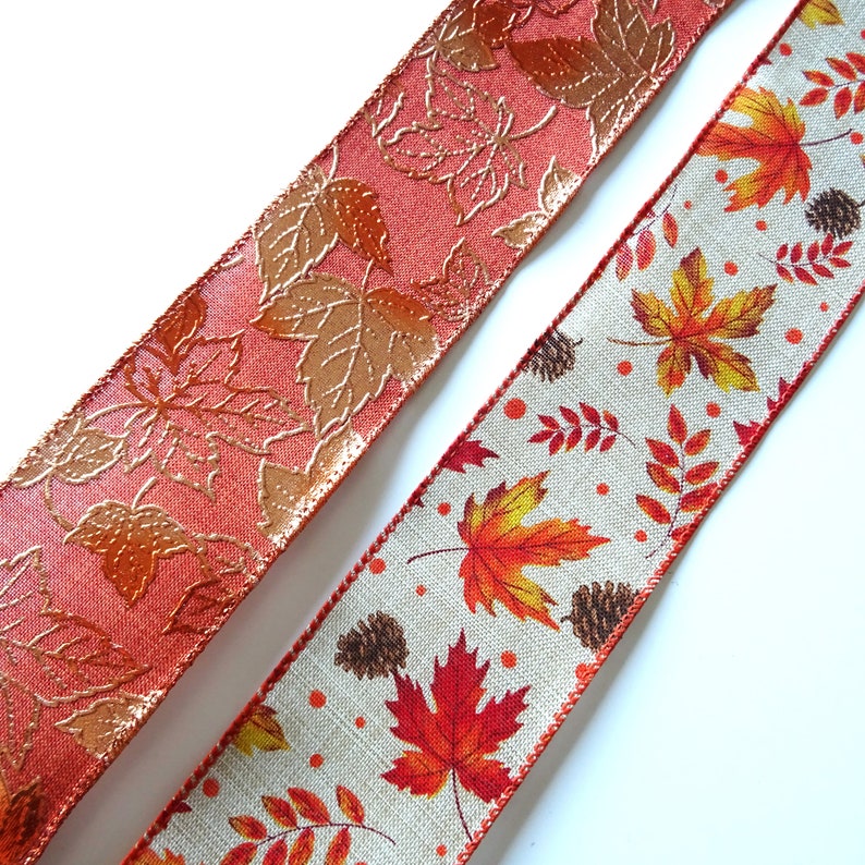 May include: Two rolls of autumn-themed ribbon. One roll is a peachy-orange colour with a gold embossed leaf pattern. The other roll is a beige linen fabric with a colourful leaf print.