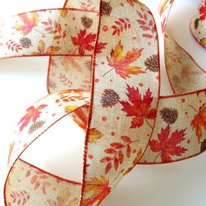 May include: A beige ribbon with a red, orange and yellow autumn leaf print. The ribbon has a subtle texture and is perfect for crafting and decorating.