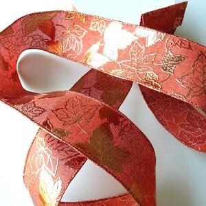 May include: A red ribbon with a gold leaf pattern. The ribbon is folded and twisted, showing the pattern on both sides.