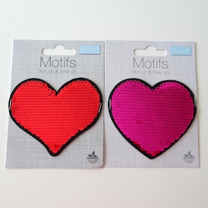 May include: Two iron-on or sew-on heart-shaped patches with sequins. The patch on the left is red and the patch on the right is pink.