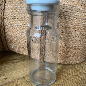 Op de afbeelding: Een glazen pot met een witte deksel. De pot heeft het woord "Pan-Yam" in reliëf aan de zijkant.