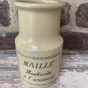 Puede incluir: Un tarro de cerámica blanco con una etiqueta negra que dice "MAILLE Mostaza a l'ancienne".