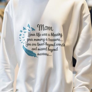 May include: White sweatshirt with a blue embroidered design featuring a feather and birds. The text reads "Mom Your life was a blessing your memory a treasure... You are loved beyond words and missed beyond measure..."