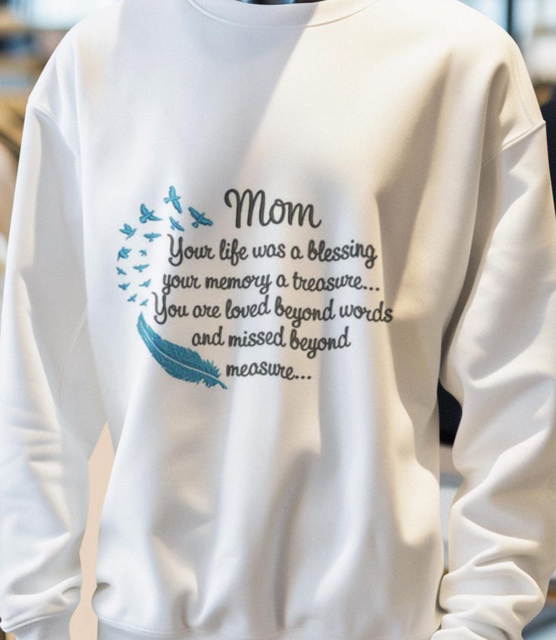 May include: White sweatshirt with a blue embroidered design featuring a feather and birds. The text reads "Mom Your life was a blessing your memory a treasure... You are loved beyond words and missed beyond measure..."