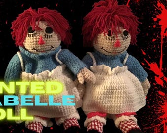 May include: Two crocheted rag dolls with red yarn hair, blue and white dresses, and red and white checkered shoes. The dolls are posed standing on a black background with red splatters.
