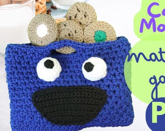Op de afbeelding: Blauwe gehaakte tas met een glimlachend gezicht, twee witte ogen met zwarte pupillen en een zwarte mond. De tas is gevuld met gehaakte koekjes in verschillende kleuren.