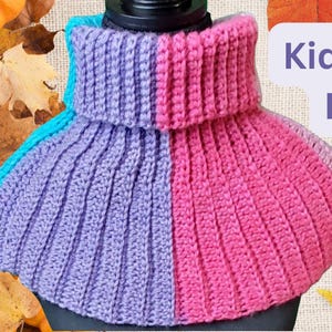 May include: A knitted dickey in shades of purple, pink, and teal. The dickey is ribbed and has a turtleneck design. The background includes pumpkins and fall leaves. Text on the right says "Kids & a Dickey".