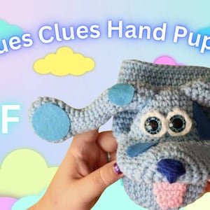 Puede incluir: Un títere de mano de crochet azul del personaje Blue's Clues. El títere tiene una lengua rosa que sobresale y manchas azules de fieltro en las orejas. El texto "Blues Clues Hand Puppet PDF" está escrito encima del títere.