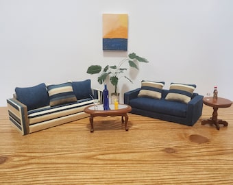 May include: Two blue striped sofas with beige cushions, a brown oval coffee table with a glass top, a small brown table with a glass top, and a potted plant with green leaves. The sofas and tables are arranged in a living room setting.