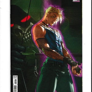 May include: A comic book titled Absolute Green Arrow #2 featuring a blonde character in a blue tank top, fishnet sleeves, and dark pants. The background shows a dark, hooded figure with glowing red eyes and a bow. The cover includes DC and All In logos.