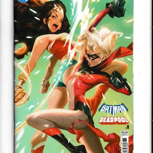 May include: Comic book cover featuring Wonder Woman and Harley Quinn in action poses. The cover has a green background with starburst effects. The title "Batman Deadpool" is visible, along with the DC and Marvel logos.