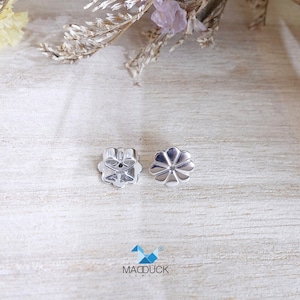 May include: Two silver earring backs in the shape of a flower. The backs have a small hole in the center for the earring post.