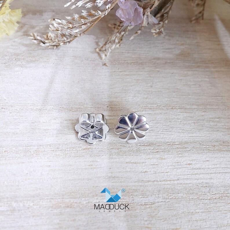 May include: Two silver earring backs in the shape of a flower. The backs have a small hole in the center for the earring post.