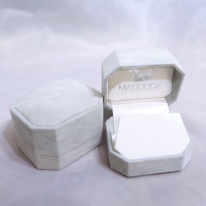May include: Two gray, octagonal-shaped boxes with a white interior. The box on the right is open and has the text "MADDUCK" printed on the inside.