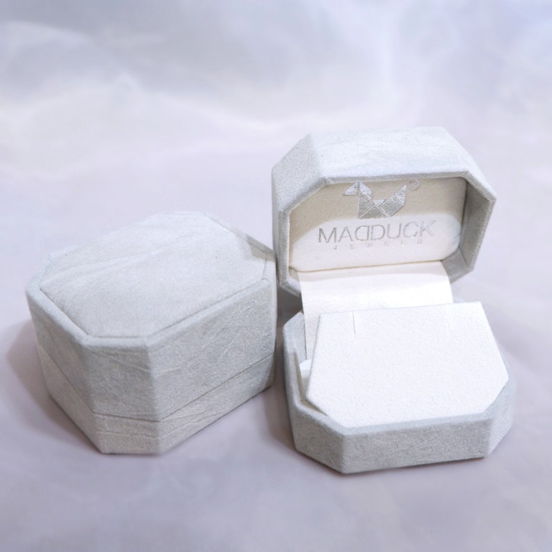 May include: Two gray, octagonal-shaped boxes with a white interior. The box on the right is open and has the text "MADDUCK" printed on the inside.