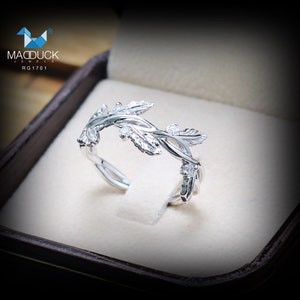 May include: A silver ring with a delicate vine design featuring leaves and small stones. The ring is displayed in a brown box with the text "MACDUCK JEWELS RG1701".
