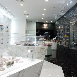May include: The interior of a jewellery store with white marble floors and walls. The store features a display case with jewellery boxes and a sign that reads "Madebuck Jewellery".