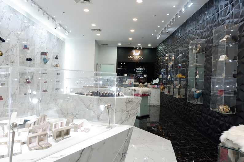 May include: The interior of a jewellery store with white marble floors and walls. The store features a display case with jewellery boxes and a sign that reads "Madebuck Jewellery".