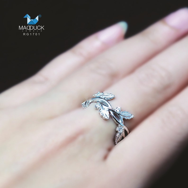 May include: A silver ring with a delicate design of intertwined leaves. The ring is on a finger, showcasing the intricate details of the leaves.