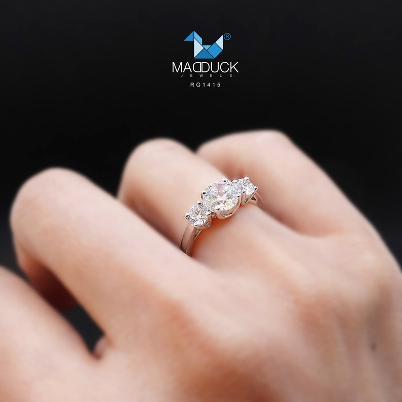 May include: A silver ring with three round diamonds set in a three-stone design. The ring is on a person's finger.
