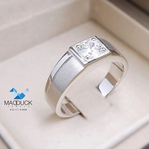 May include: A silver ring with a square-shaped setting featuring a clear, round gemstone. The ring is in a white box with the text "MADDUCK JEWELS RG1716 WGR" on the bottom.