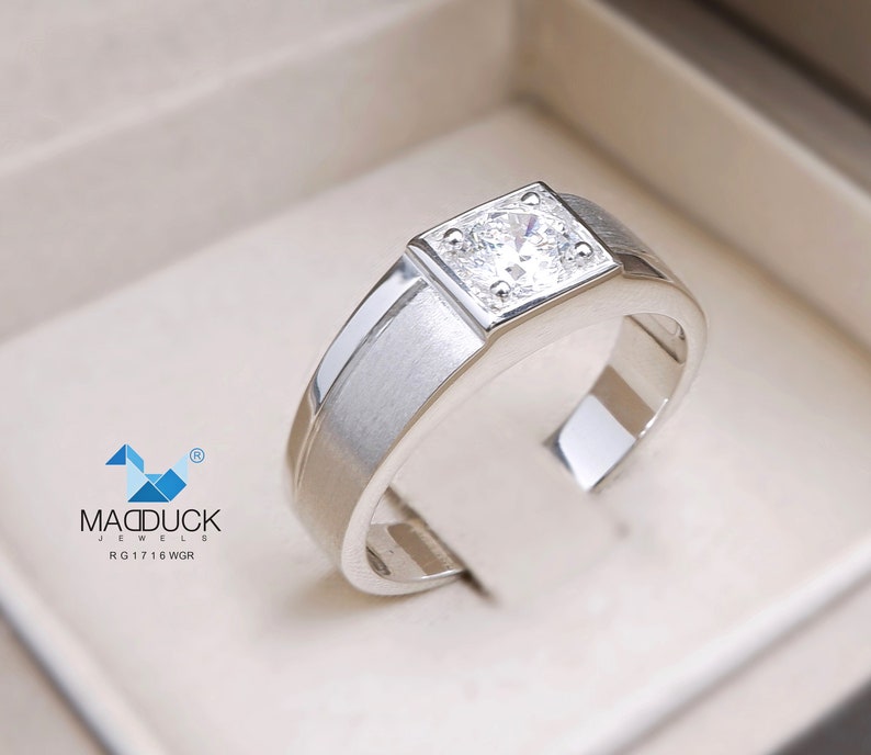 May include: A silver ring with a square-shaped setting featuring a clear, round gemstone. The ring is in a white box with the text "MADDUCK JEWELS RG1716 WGR" on the bottom.