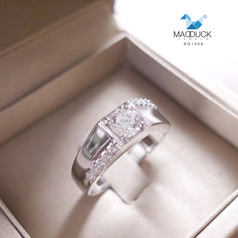 May include: A silver ring with a square-shaped center stone and smaller stones set around the band. The ring is in a white box with the text "MADDUCK JEWELS RG1559".