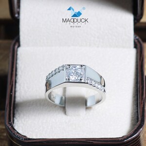 May include: A silver men's ring with a square-shaped center stone and smaller stones set along the band. The ring is in a white box with the text "MADDUCK JEWELS RG1559".