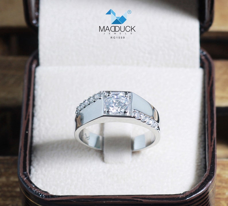 May include: A silver men's ring with a square-shaped center stone and smaller stones set along the band. The ring is in a white box with the text "MADDUCK JEWELS RG1559".