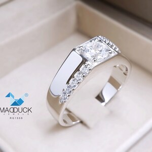 May include: A silver ring with a large, clear, round gemstone surrounded by smaller, clear gemstones. The ring is set in a square-shaped band.