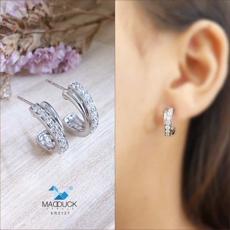 May include: Silver hoop earrings with a double row of clear cubic zirconia stones. The earrings are shown on a model's ear.