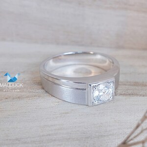 May include: A silver band with a square-shaped diamond set in a square bezel. The band has a brushed finish and a thin polished line around the edge.
