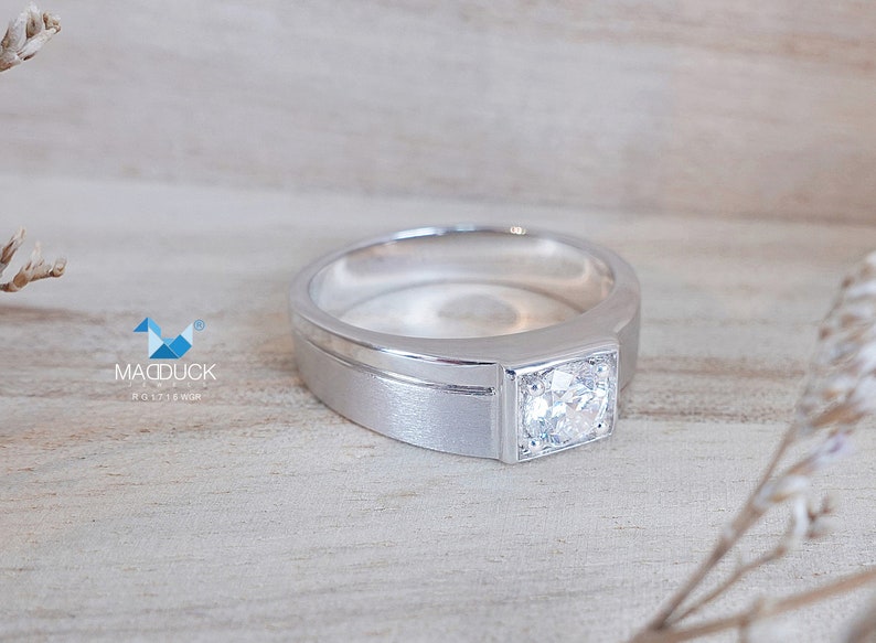 May include: A silver band with a square-shaped diamond set in a square bezel. The band has a brushed finish and a thin polished line around the edge.