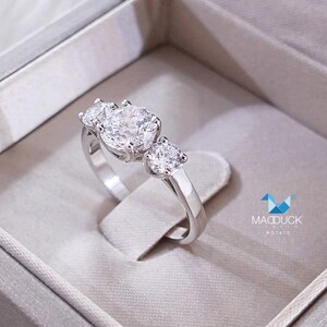 May include: A silver ring with three round diamonds. The ring is in a white box with the text "MADDUCK JEWELS R01475".