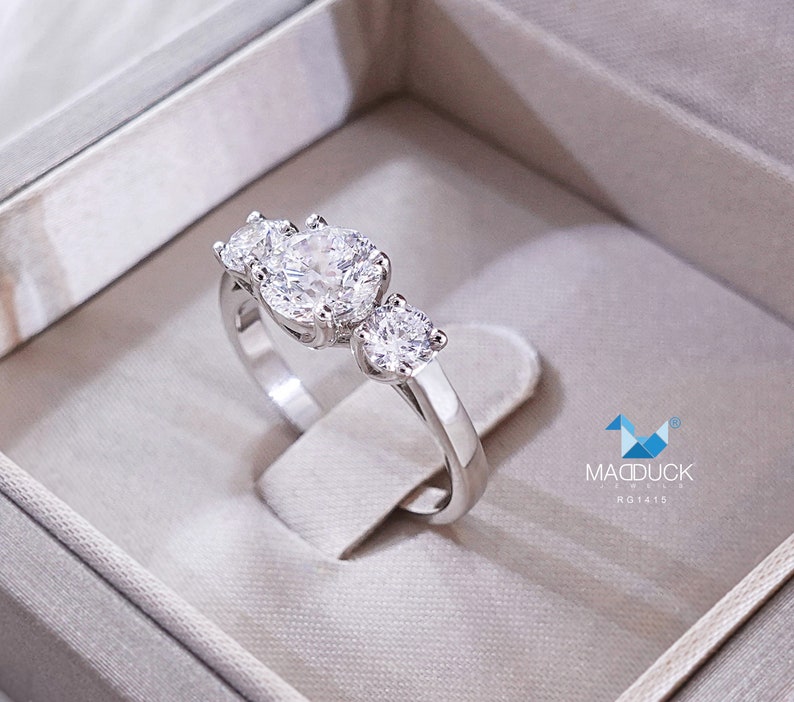 May include: A silver ring with three round diamonds. The ring is in a white box with the text "MADDUCK JEWELS R01475".