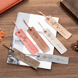 May include: Six personalized leather bookmarks with floral designs and names. The bookmarks are in various colors, including pink, brown, and silver.