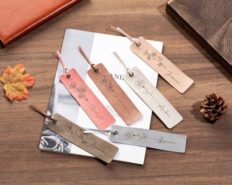 May include: Six personalized leather bookmarks with floral designs and names. The bookmarks are in various colors, including pink, brown, and silver.