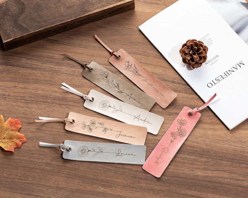 May include: Six leather bookmarks with floral designs and personalized names. The bookmarks are in shades of brown and pink with white string.