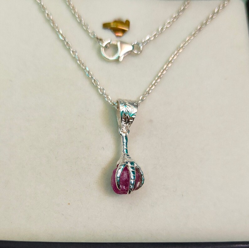 May include: A silver necklace with a claw pendant holding a pink gemstone.
