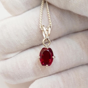 May include: A silver chain necklace with a red oval gemstone pendant.