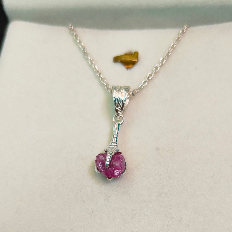 May include: A silver necklace with a pink gemstone pendant. The pendant is shaped like a claw and the gemstone is rough and unpolished.