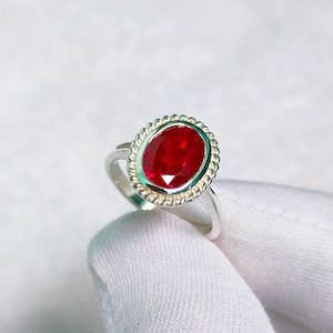 May include: A silver ring with a red oval gemstone set in a decorative silver bezel.