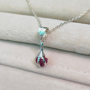 May include: A silver necklace with a pink gemstone pendant shaped like a claw.