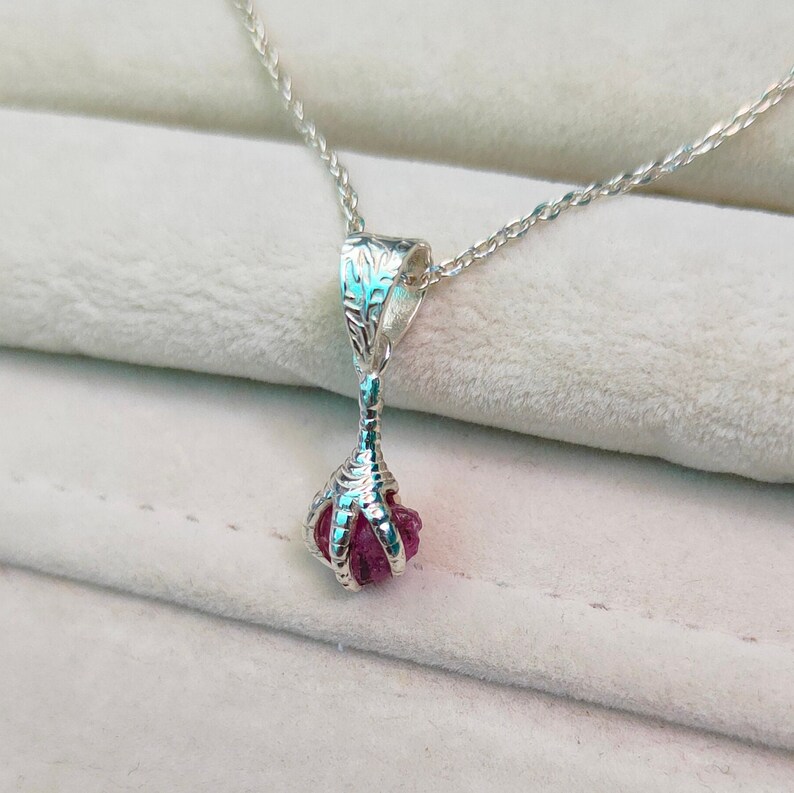 May include: A silver necklace with a pink gemstone pendant shaped like a claw.