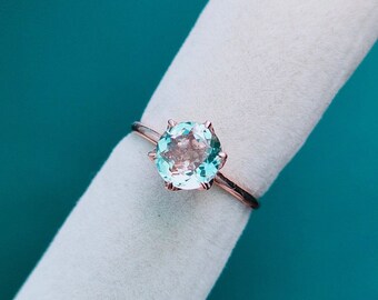 May include: A rose gold ring with a light blue gemstone set in a prong setting.