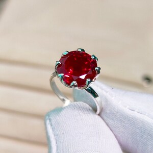 May include: A silver ring with a large, round, red ruby gemstone set in a prong setting.