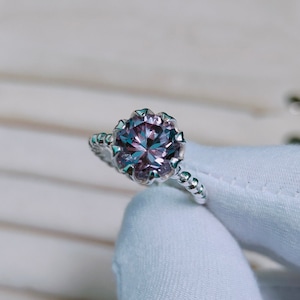 May include: A silver ring featuring a large, round, purple and green gemstone set in a crown-like setting.